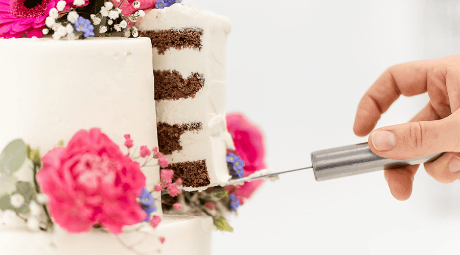 Hand schneidet eine mehrstöckige Hochzeitstorte mit Blumenverzierung.